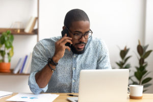 A man makes a phone call while working on his laptop,