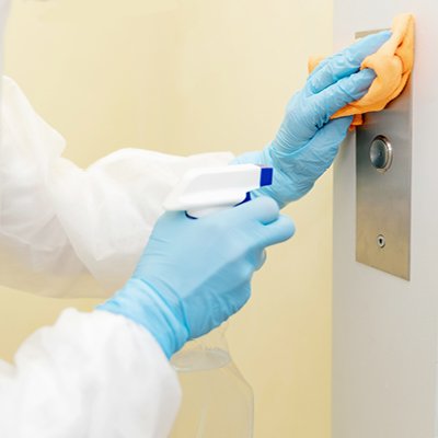 A person wearing PPE cleans an elevator button.